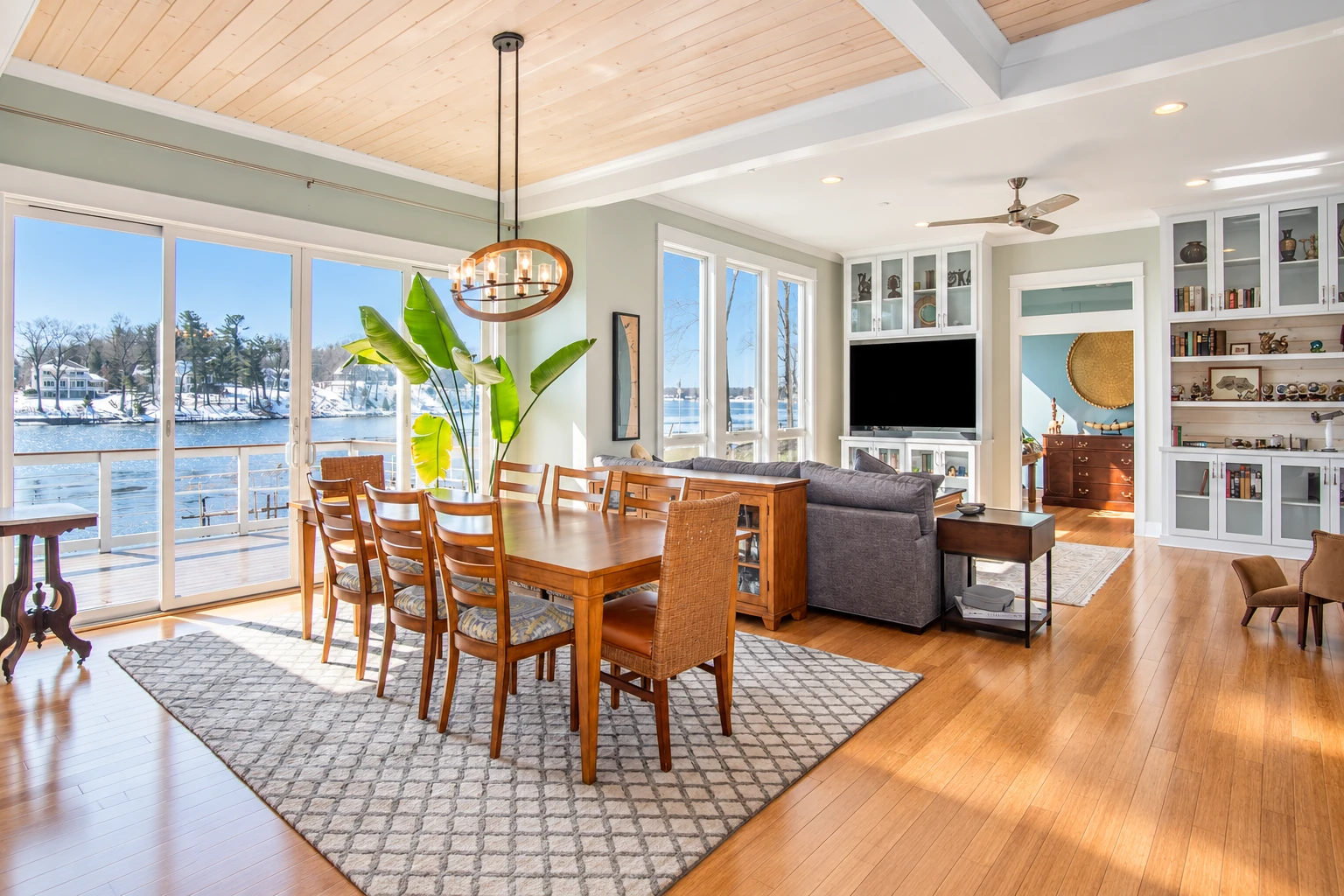 Open-plan sunroom with broad windows, a wood dining table and views of a snowy lakeside.