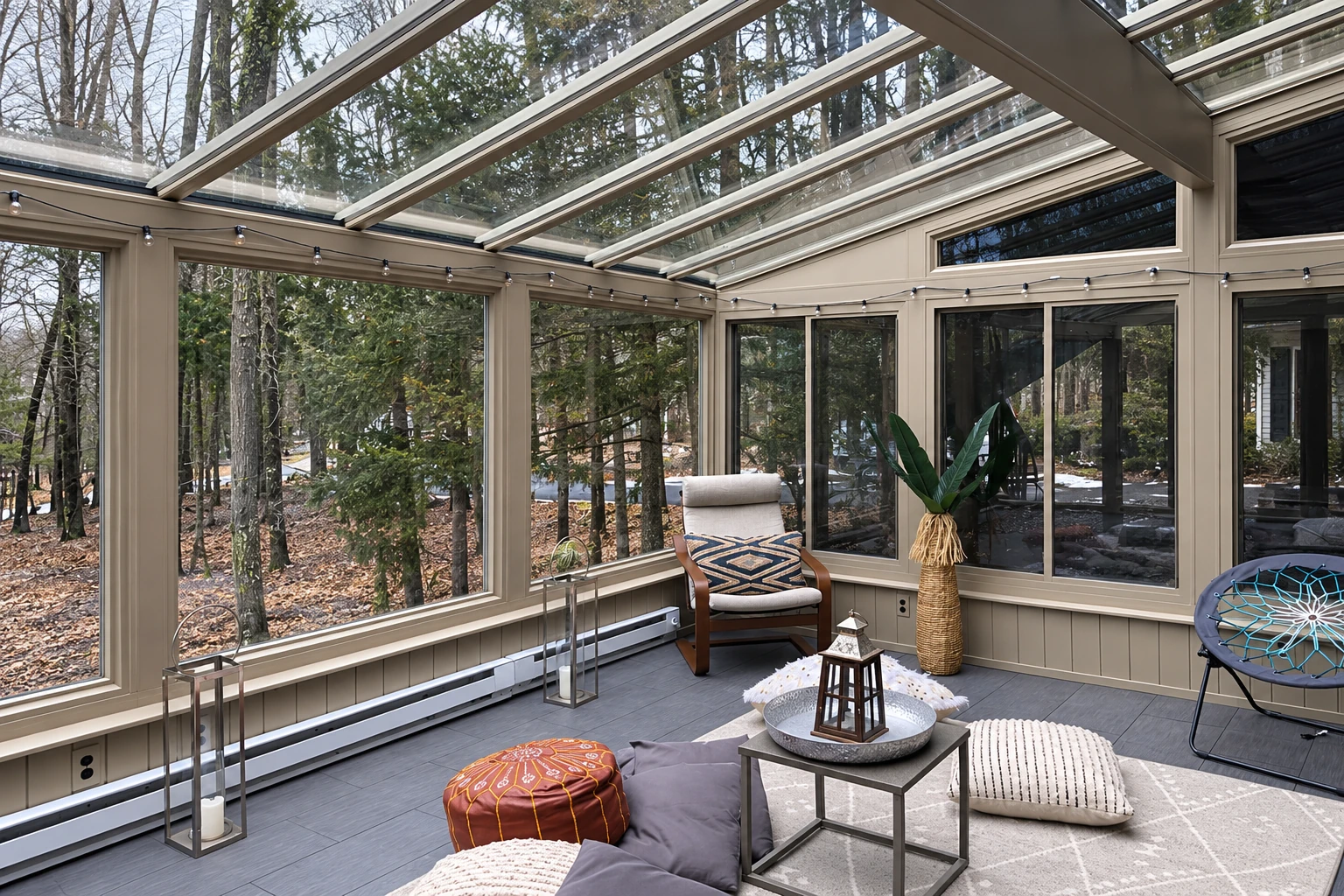 A furnished solarium has glass walls and a transparent roof, with a lounge chair and trees visible outside.