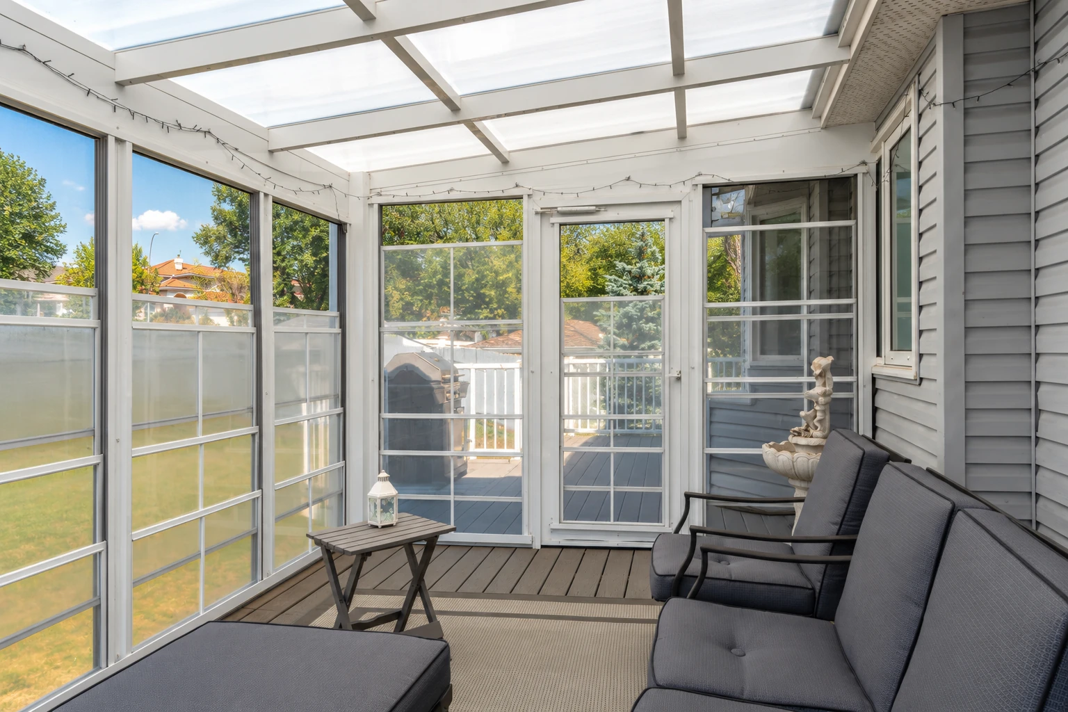 Three-season sunroom with screened windows, a translucent roof, and dark lounge seating beside a small table.